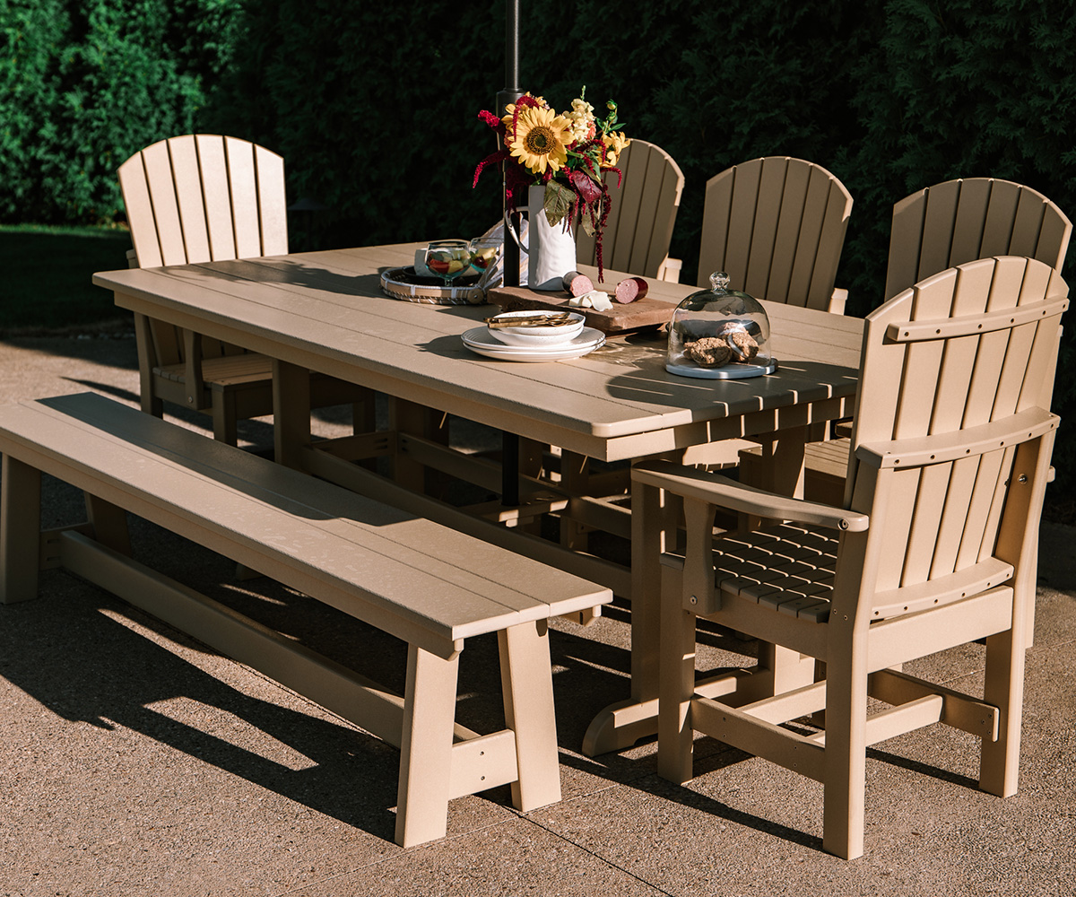 A stylish outdoor dining set featuring a large wooden table, matching Adirondack-style chairs, and a bench, beautifully set with plates, appetizers, and a floral centerpiece, creating a warm and inviting patio space.