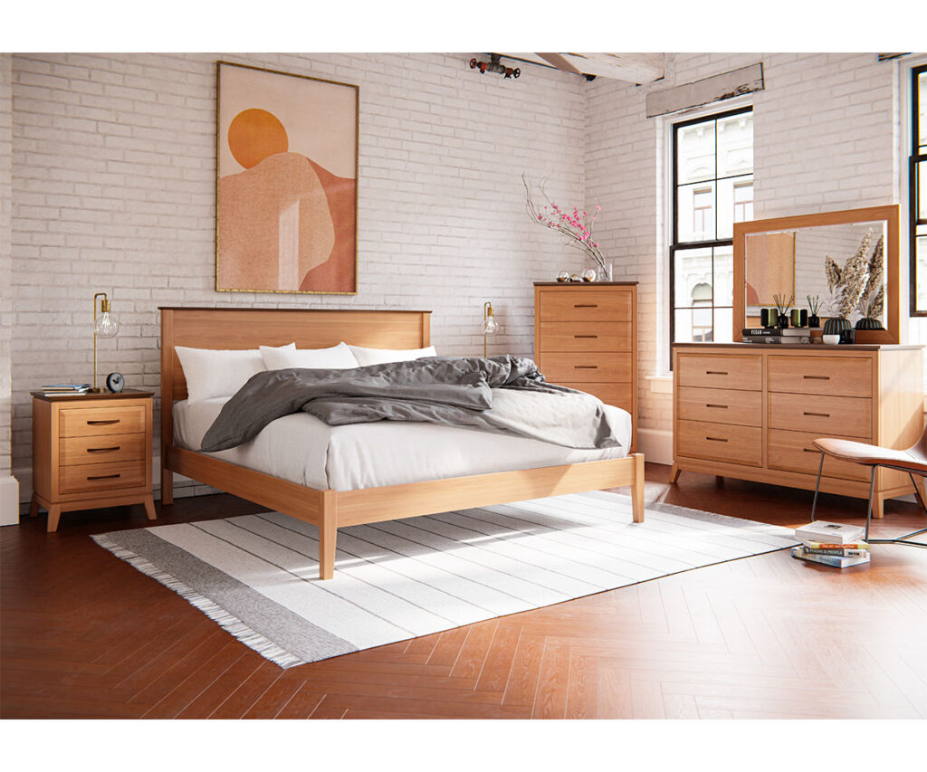 Modern bedroom with light cherry wood furniture including a bed frame, nightstand, dresser, and tall chest against white brick walls. The space is decorated with minimalist elements like a framed abstract print and a striped area rug, bathed in natural light from large windows.
