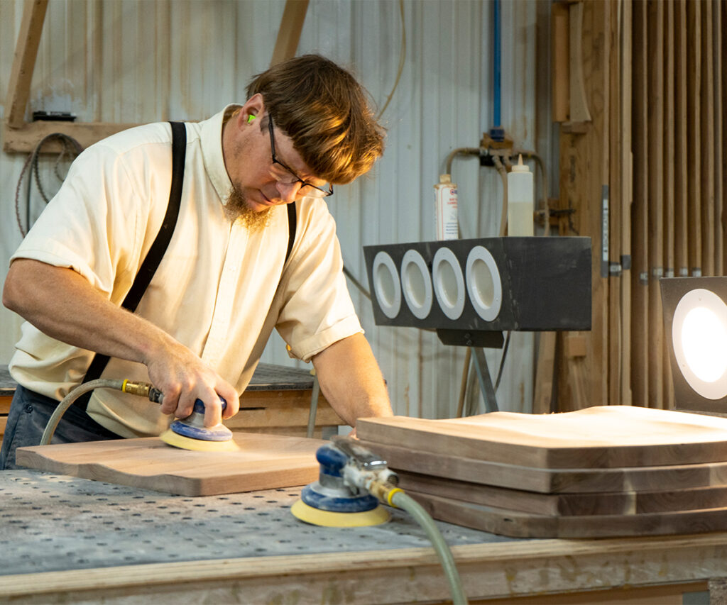 Amish quality furniture builder sanding solid wood tabletop.