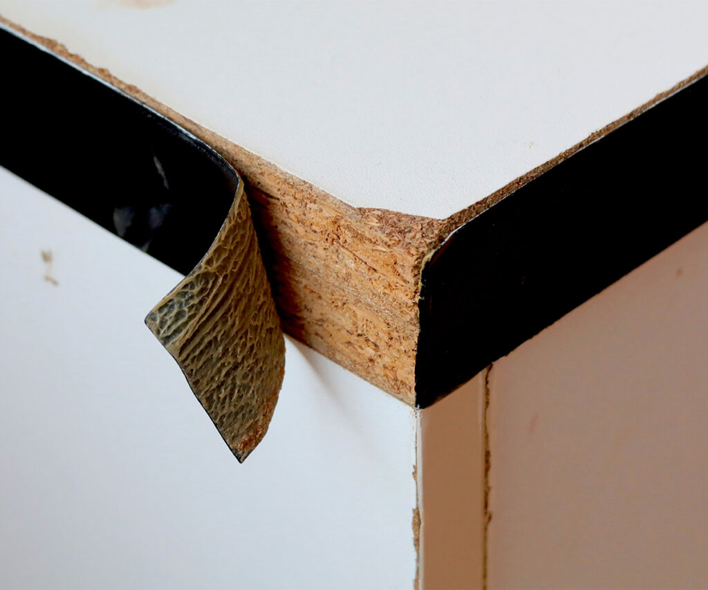 Peeling laminate reveals particleboard core on cabinet edge.