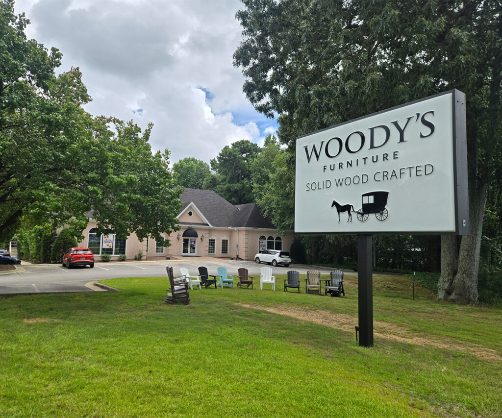 Woody’s Furniture Raleigh showroom sign on lawn with building in background.